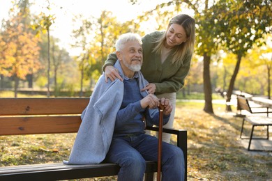 Caregiver assisting senior man on wooden bench in park. Home health care service