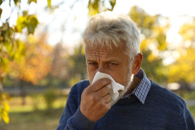 Senior man with runny nose in park, space for text