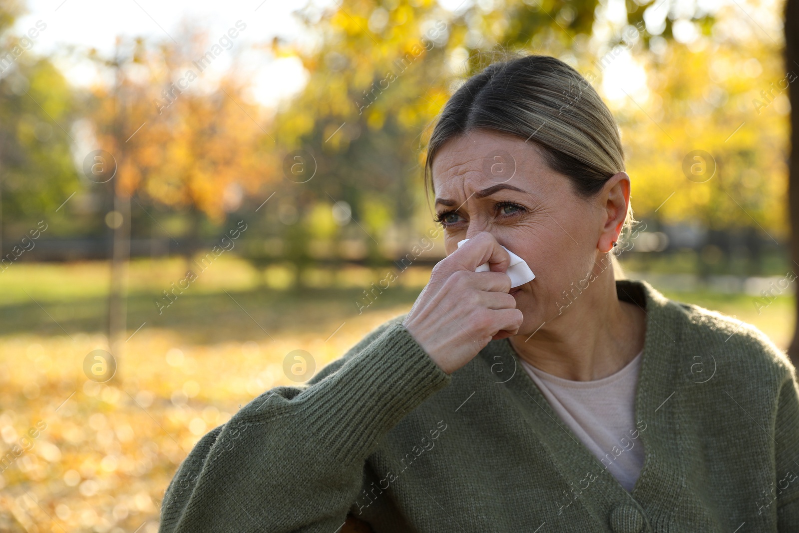 Photo of Woman with tissue blowing runny nose in park