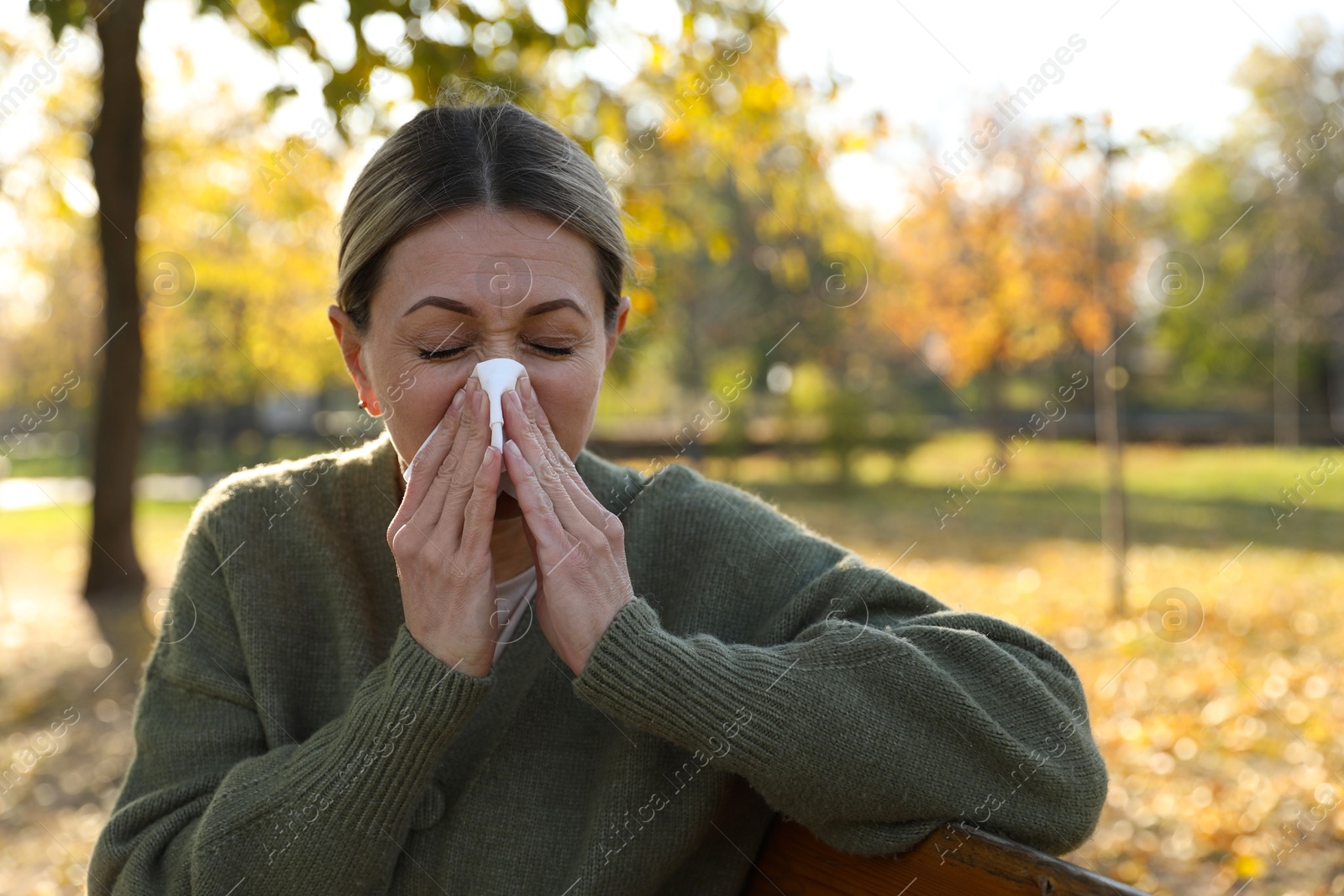 Photo of Woman with tissue blowing runny nose in park