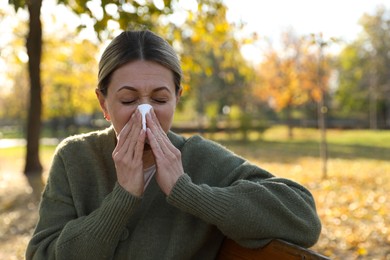 Woman with tissue blowing runny nose in park