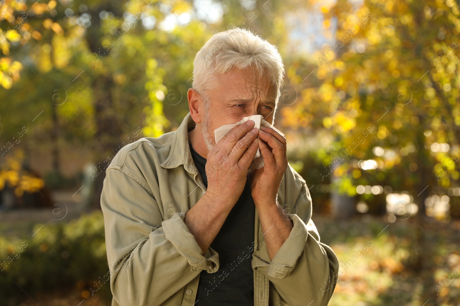 Photo of Senior man with tissue blowing runny nose in park