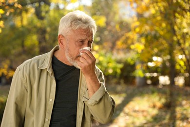 Senior man with runny nose in park, space for text