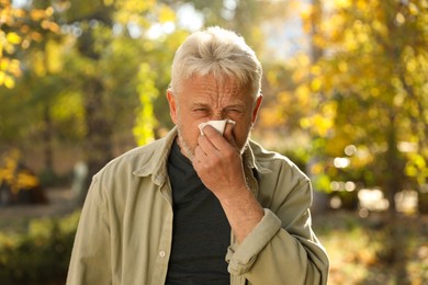 Photo of Senior man with tissue blowing runny nose in park