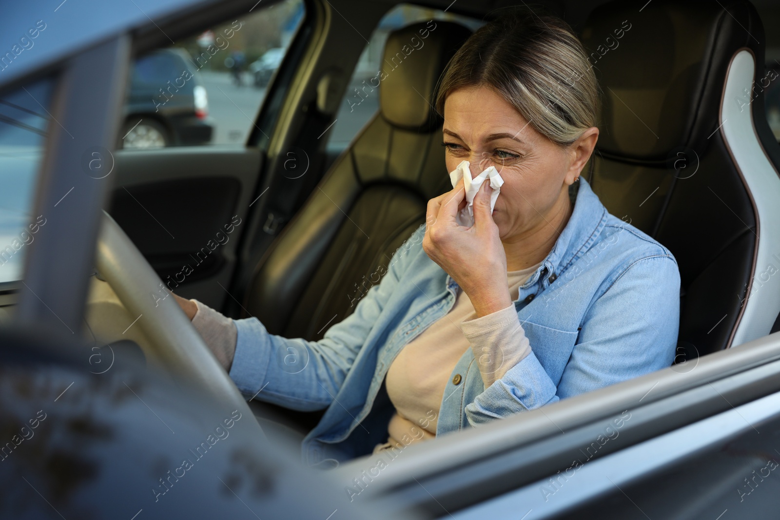 Photo of Woman with tissue blowing runny nose in car