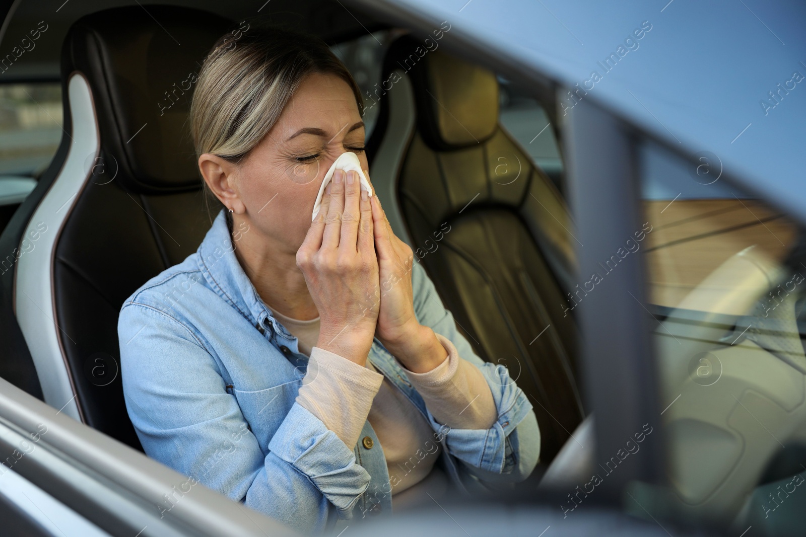 Photo of Woman with tissue blowing runny nose in car