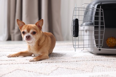 Photo of Adorable dog and pet carrier on floor indoors