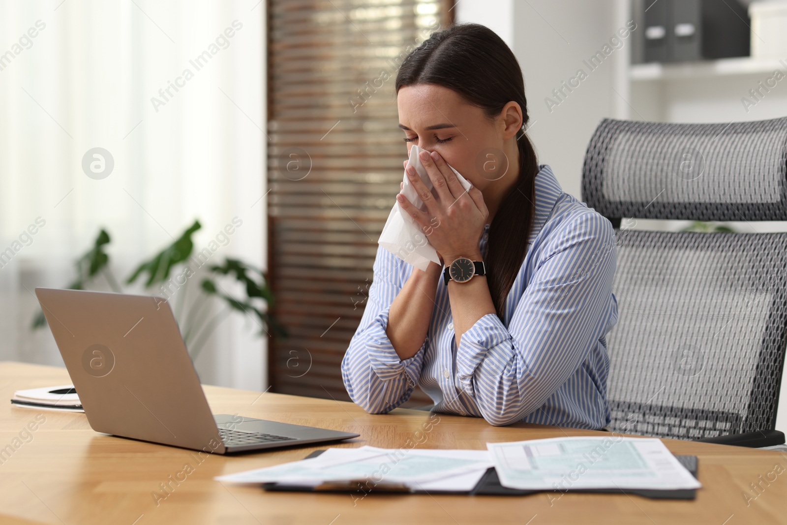 Photo of Sick woman with runny nose at table in office