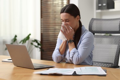 Sick woman with runny nose at table in office