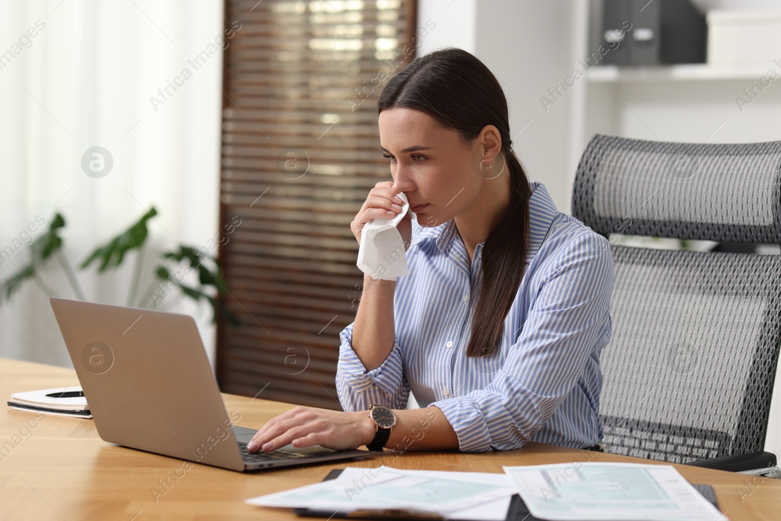 Photo of Sick woman with runny nose working at table in office