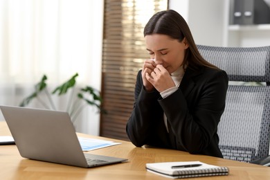 Photo of Sick woman with runny nose at table in office