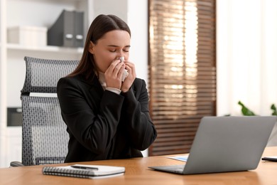 Photo of Sick woman with runny nose at table in office