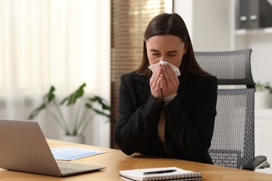 Sick woman with runny nose at table in office