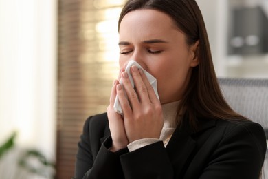 Sick woman with runny nose in office, space for text