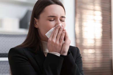 Sick woman with runny nose in office, space for text