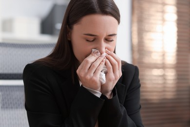 Photo of Sick woman with runny nose in office, space for text