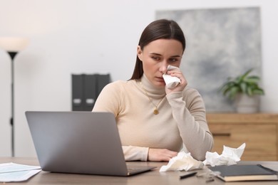 Sick woman with runny nose at table in office