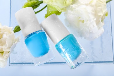 Photo of Nail polishes in bottles and beautiful flowers on light background, flat lay