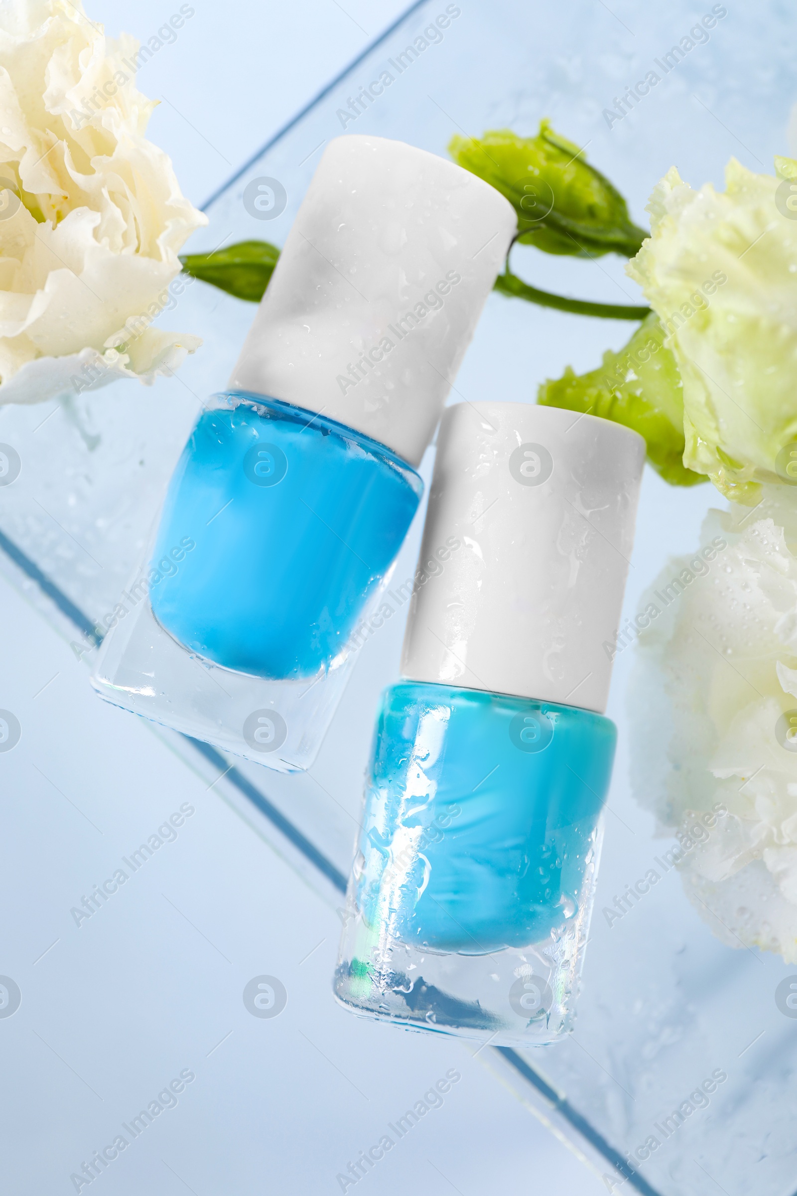 Photo of Nail polishes in bottles and beautiful flowers on light background, flat lay