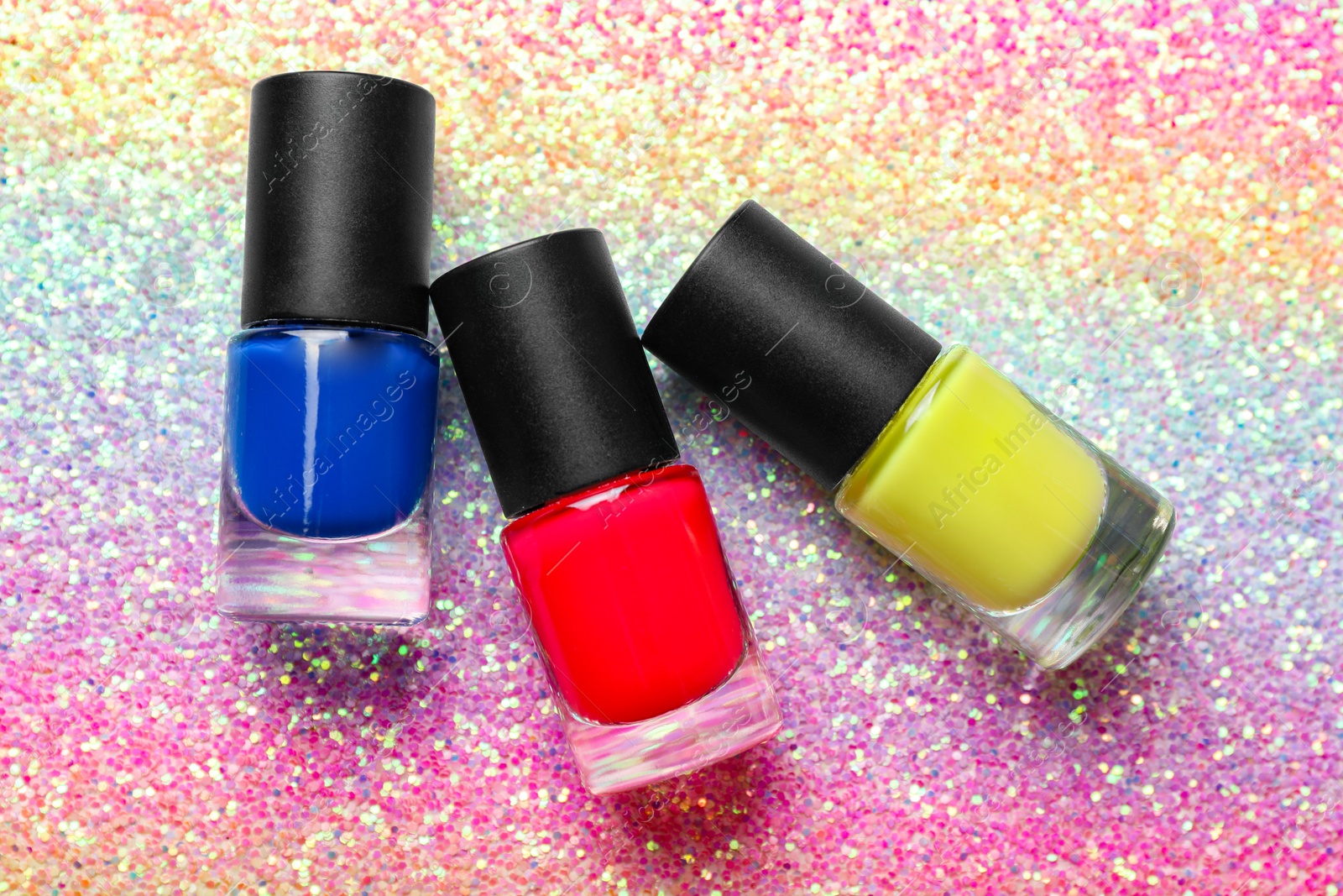 Photo of Nail polishes in bottles on bright textured surface, flat lay