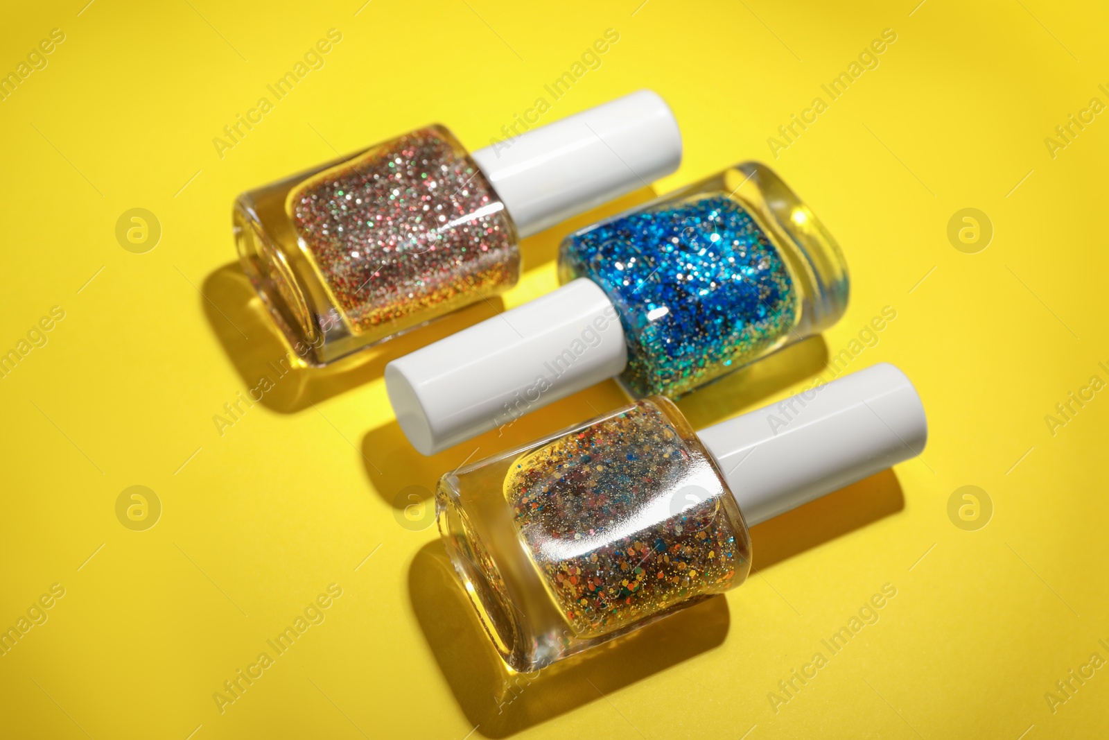 Photo of Nail polishes in bottles on yellow background, closeup