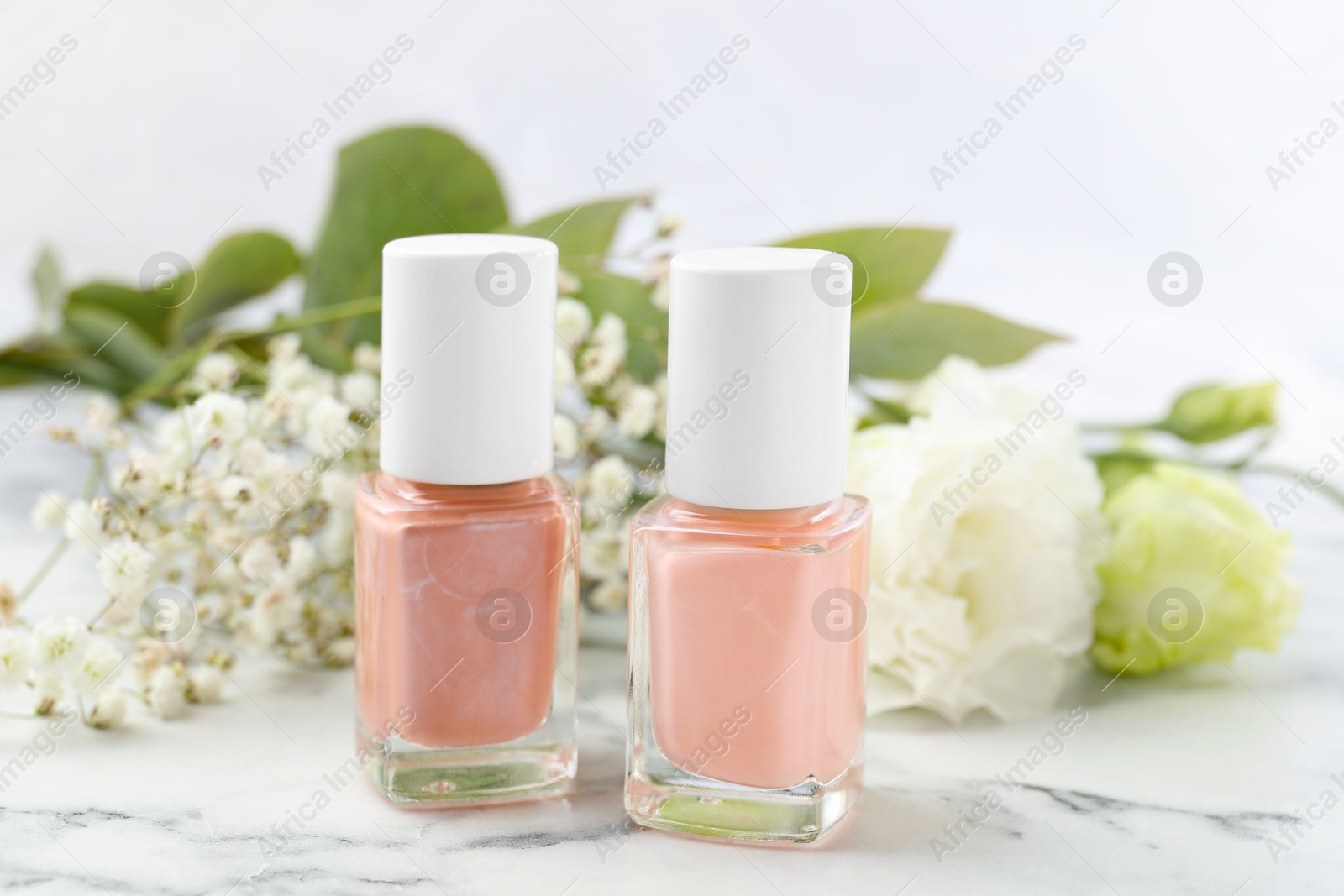 Photo of Nail polishes in bottles on white marble table, closeup