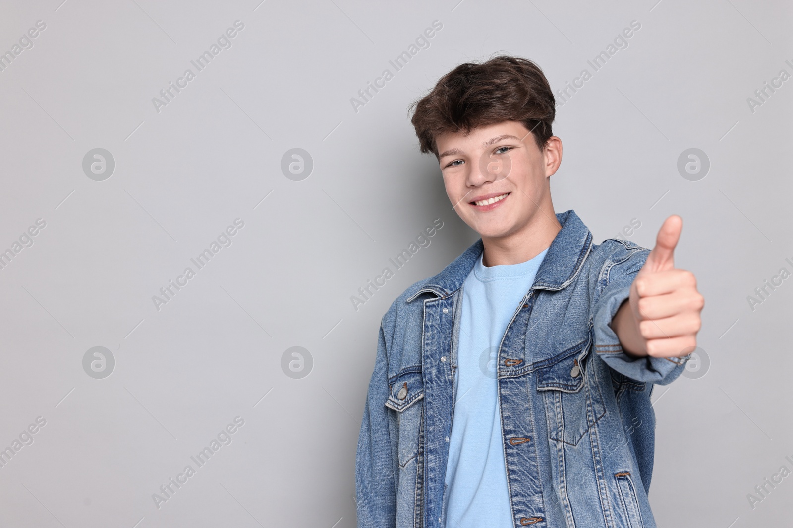 Photo of Happy teenage boy showing thumbs up on light grey background, space for text