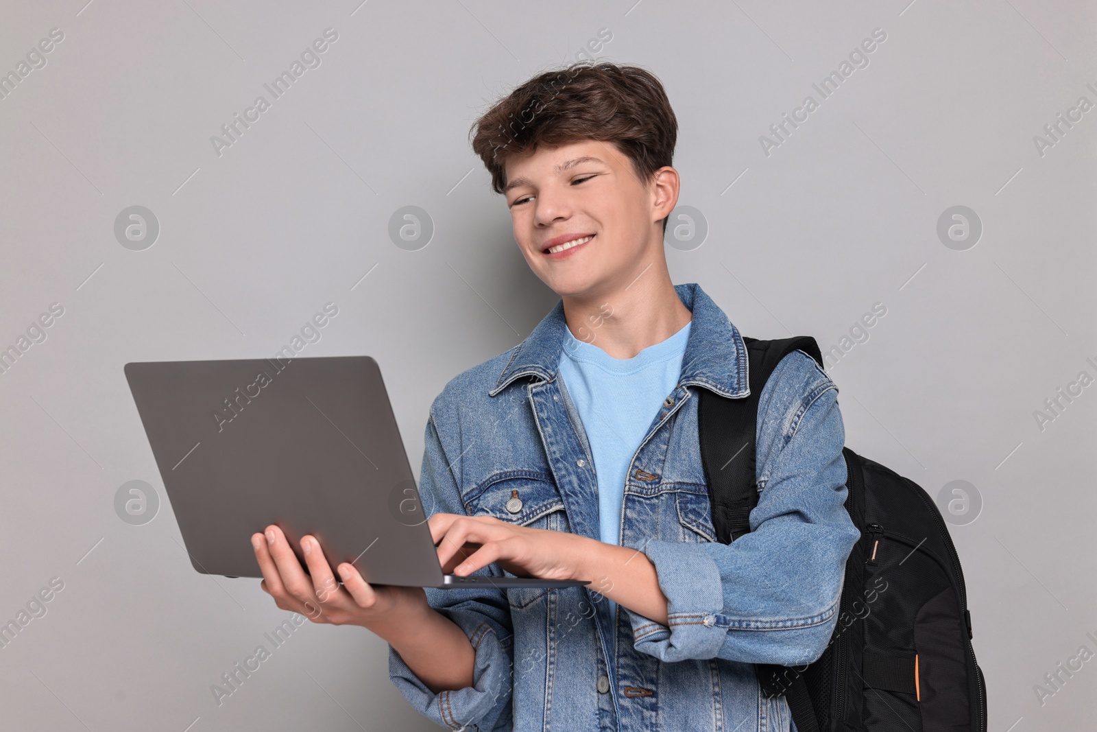 Photo of Happy teenage boy with laptop and backpack on light grey background