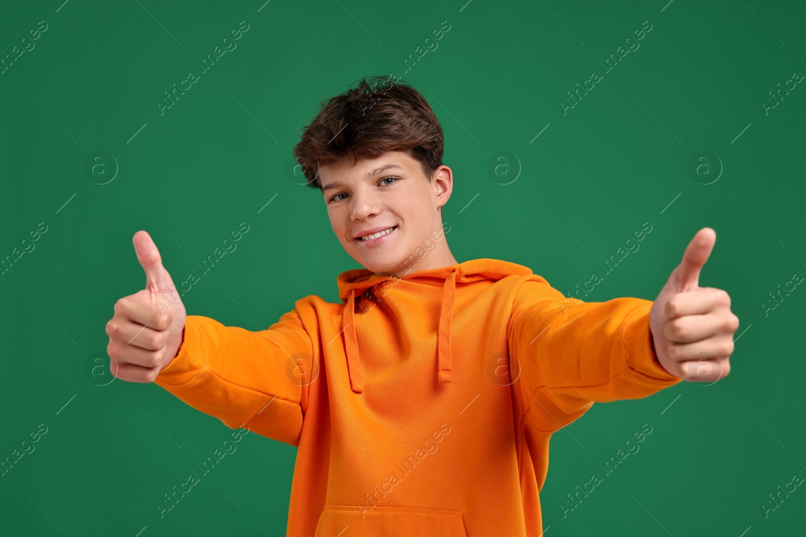 Photo of Happy teenage boy showing thumbs up on green background