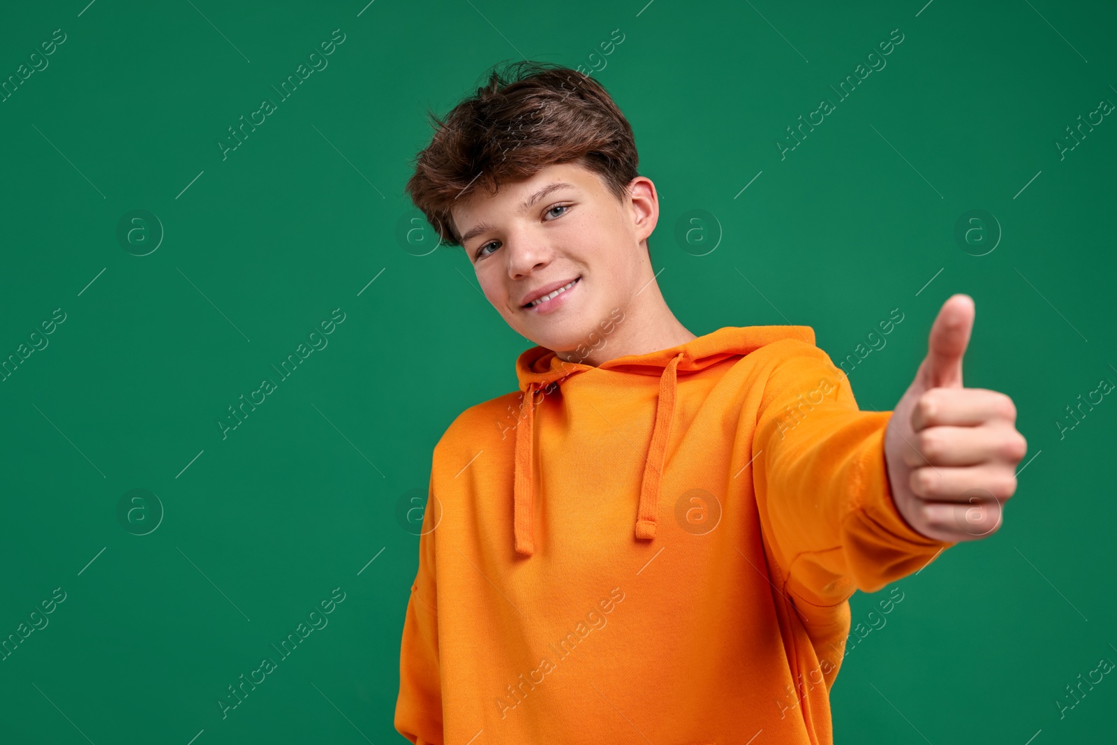 Photo of Happy teenage boy showing thumbs up on green background