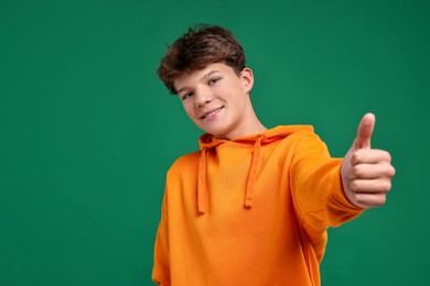 Photo of Happy teenage boy showing thumbs up on green background