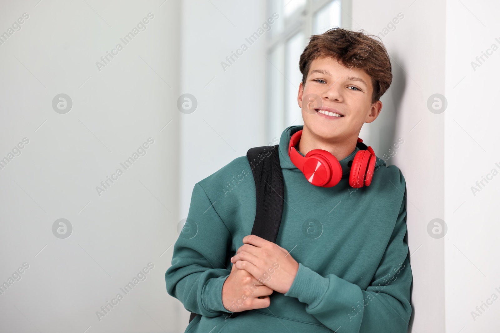 Photo of Happy teenage boy with headphones and backpack indoors, space for text