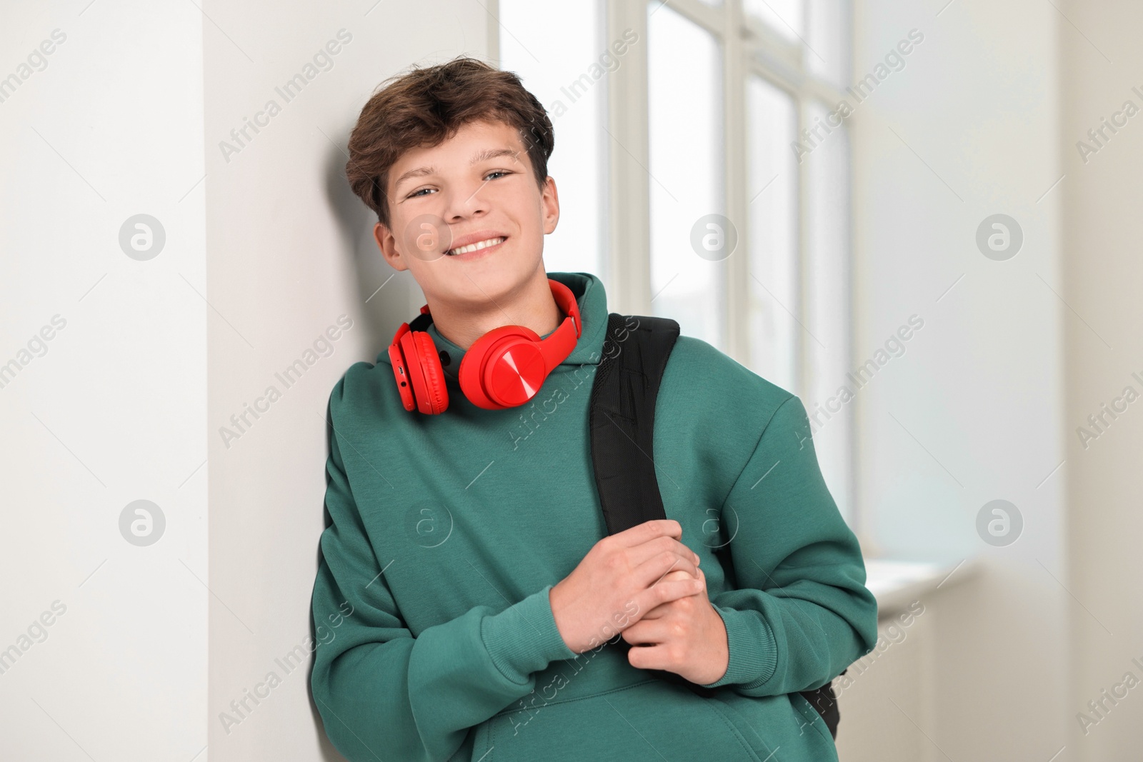 Photo of Happy teenage boy with headphones and backpack indoors