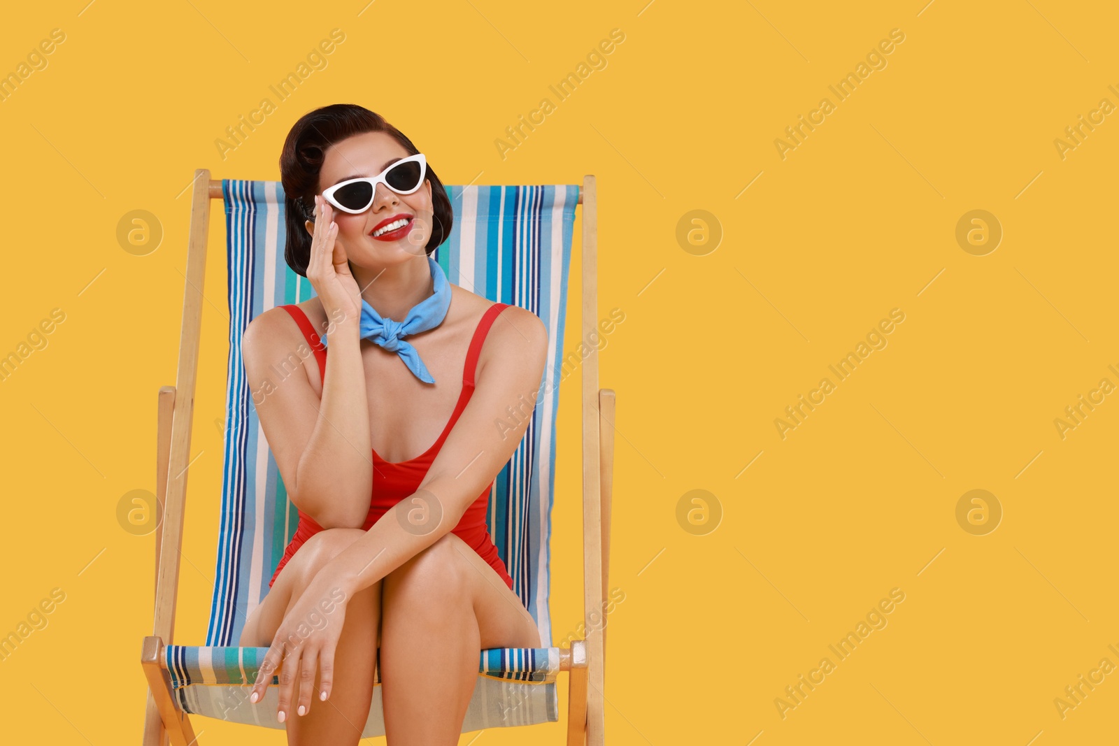 Photo of Pin-up woman in swimsuit on folding chair against orange background, space for text