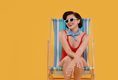 Photo of Pin-up woman in swimsuit on folding chair against orange background