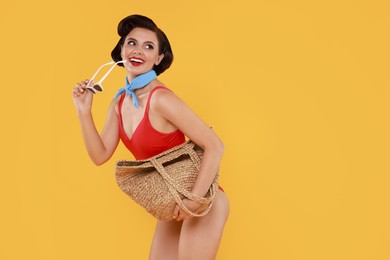 Photo of Pin-up woman in swimsuit with beach bag on orange background, space for text