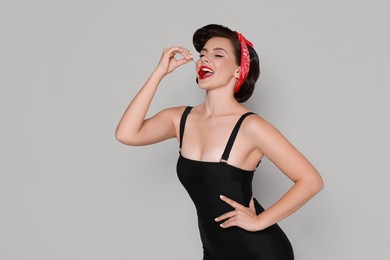 Pin-up woman eating cherry on grey background