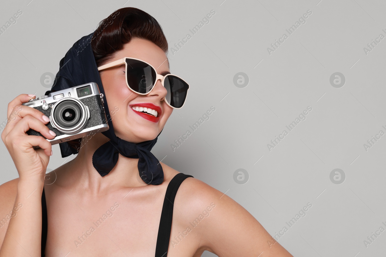 Photo of Pin-up woman in sunglasses with camera on grey background, space for text