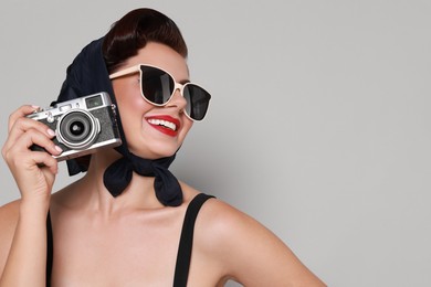 Photo of Pin-up woman in sunglasses with camera on grey background, space for text