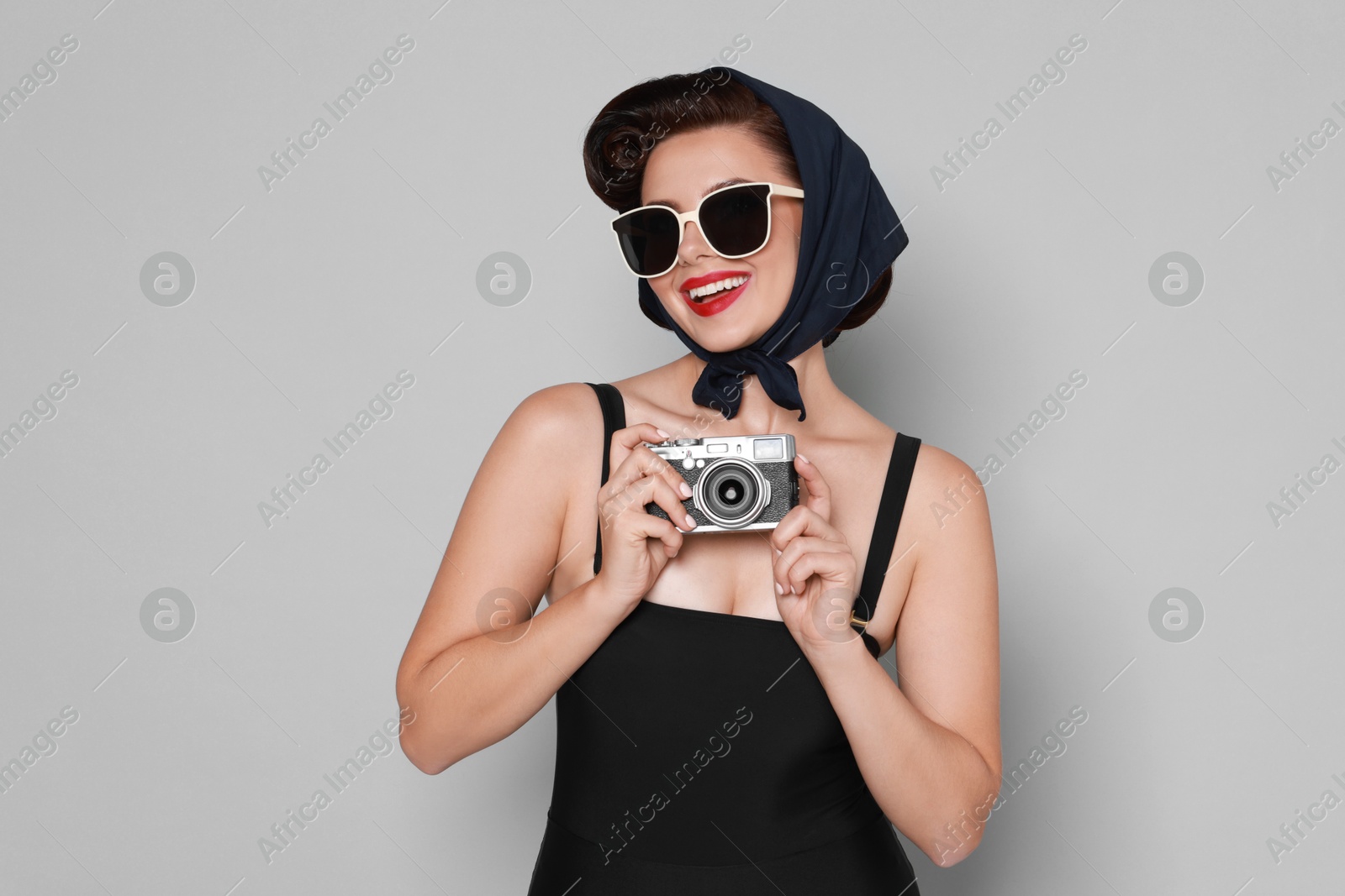 Photo of Pin-up woman in sunglasses with camera on grey background