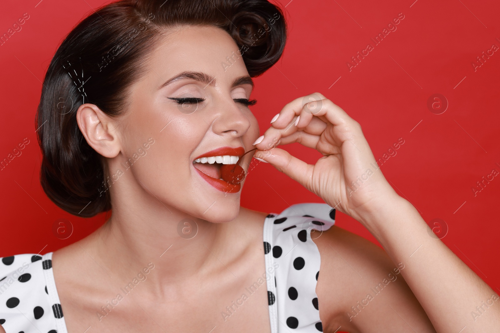 Photo of Pin-up woman eating cherry on red background