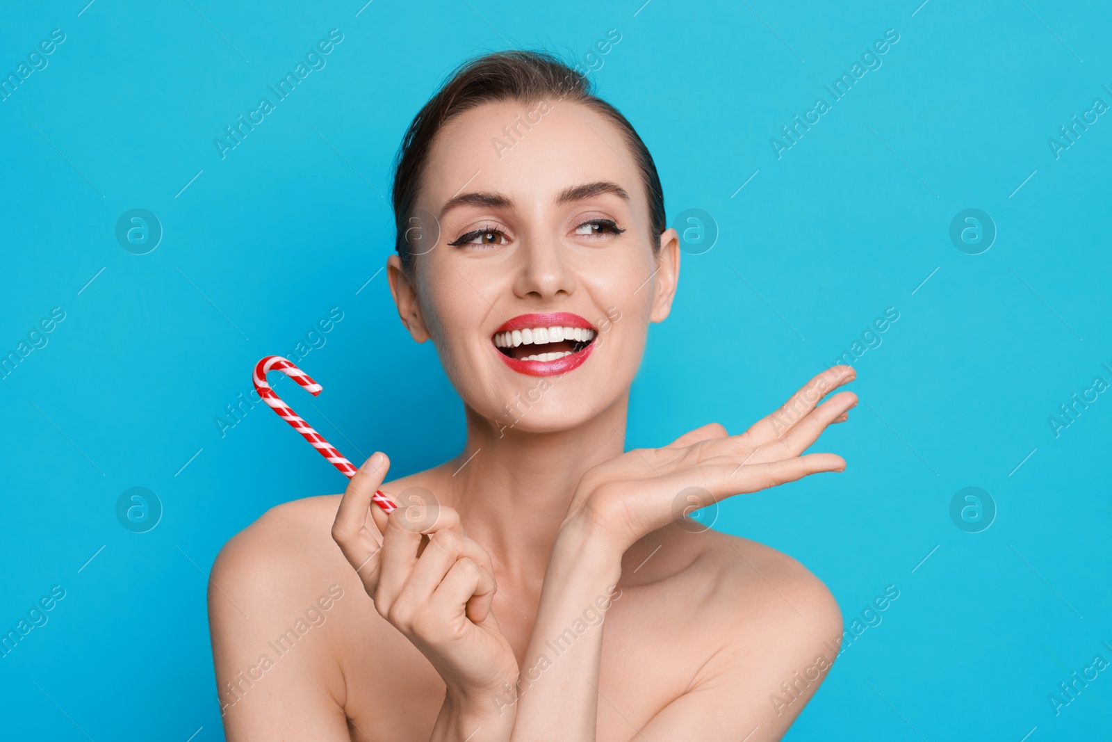 Photo of Smiling woman with perfect makeup holding Christmas candy cane on light blue background