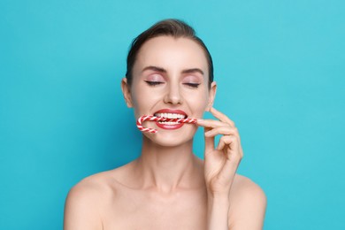 Woman with Christmas candy cane on light blue background