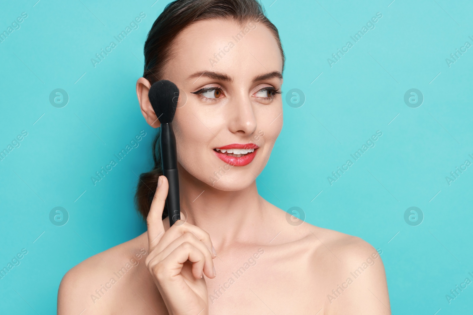 Photo of Smiling woman with makeup brush on light blue background