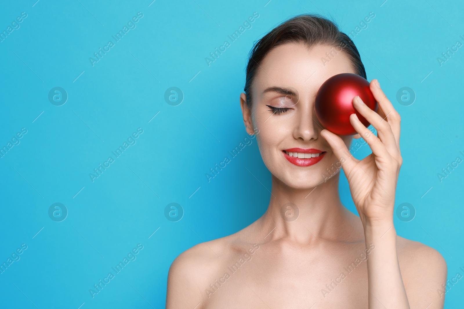 Photo of Smiling woman with perfect makeup holding Christmas bauble on light blue background. Space for text