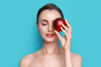 Photo of Woman with perfect makeup holding Christmas bauble on light blue background