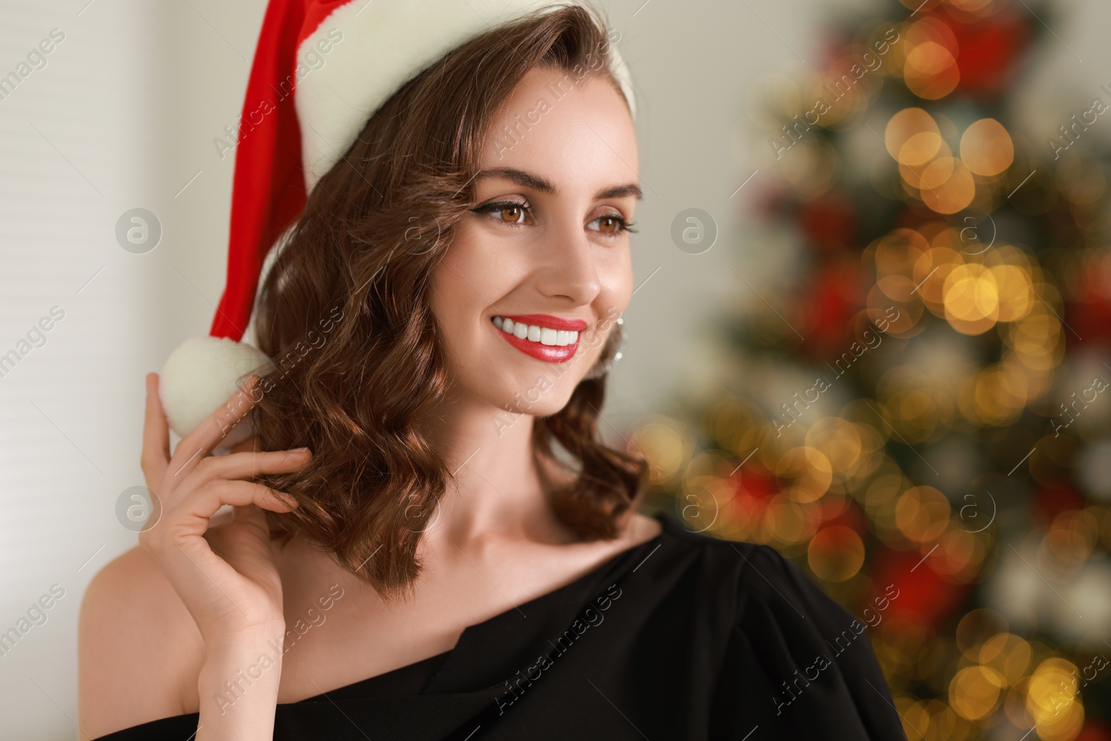 Photo of Smiling woman with perfect makeup in Santa hat celebrating Christmas at home