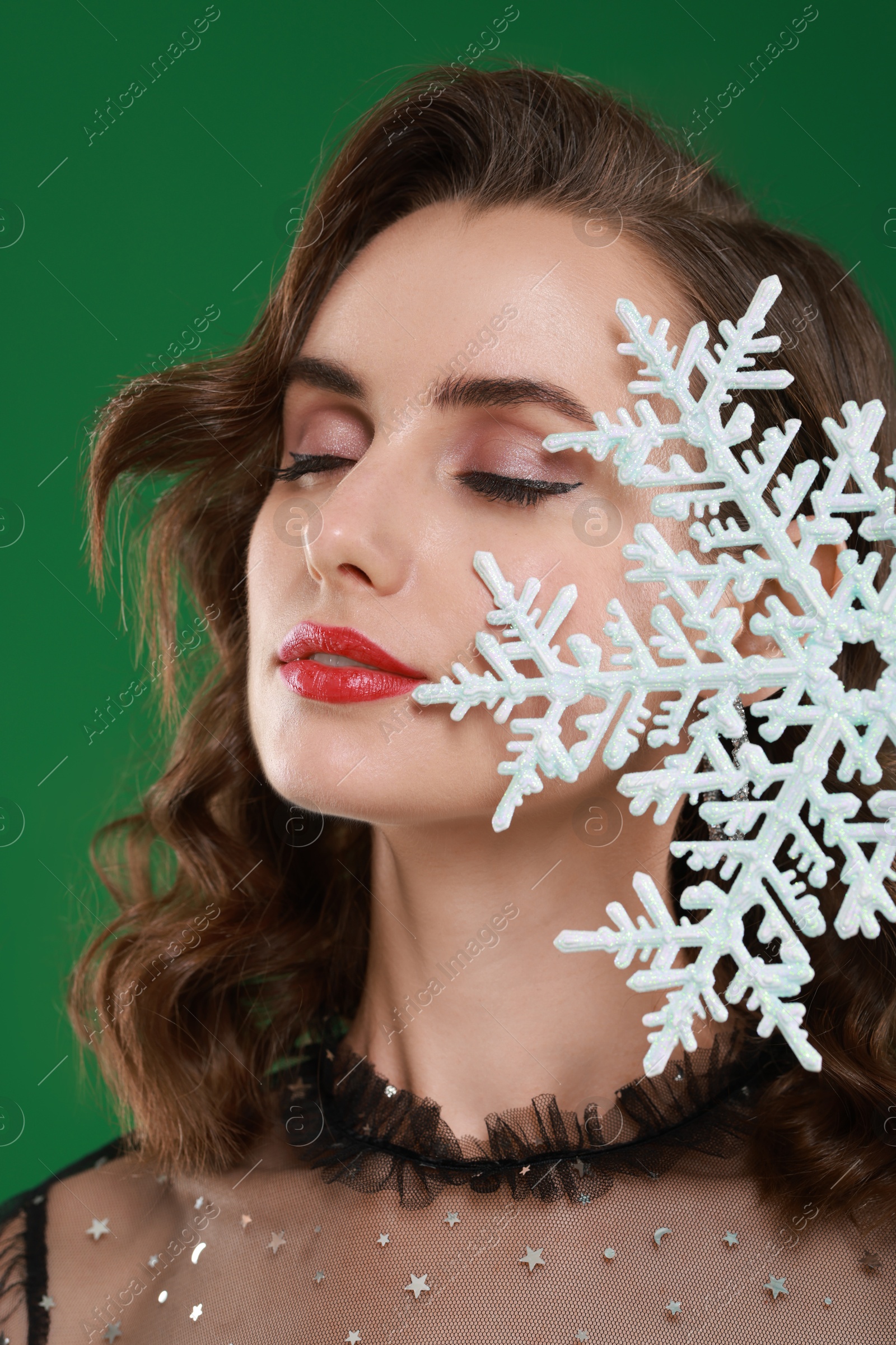 Photo of Woman with perfect makeup holding decorative snowflake on green background. Christmas celebration