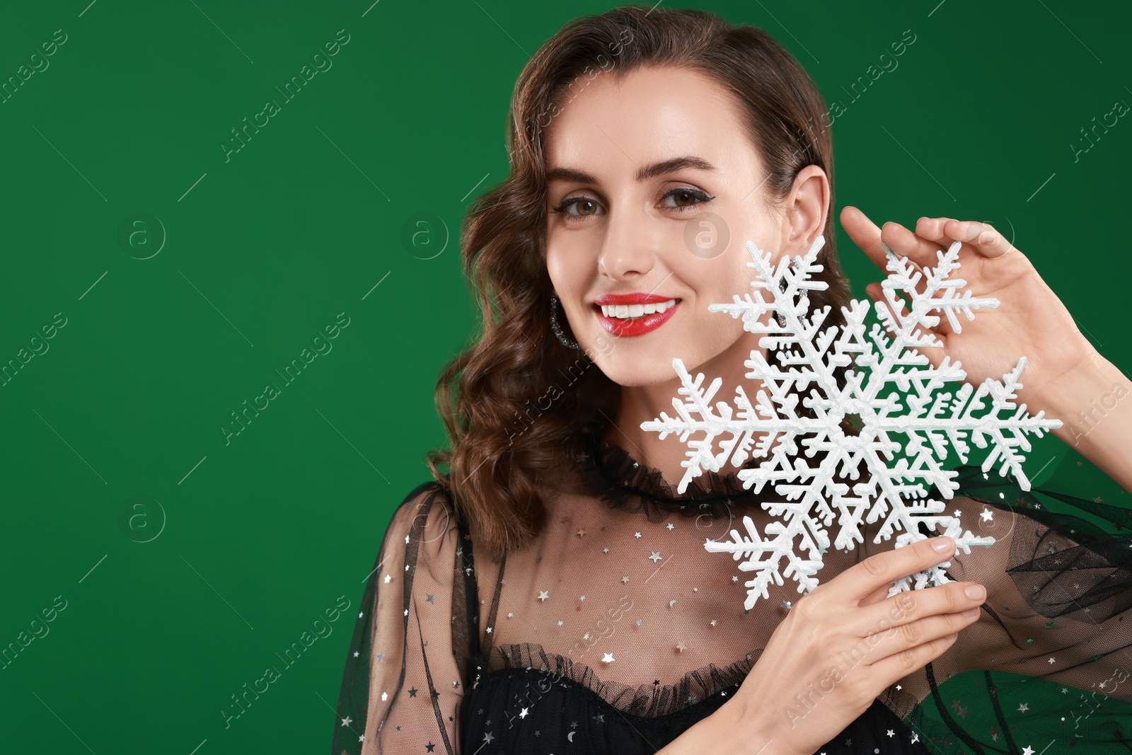 Photo of Smiling woman with perfect makeup holding decorative snowflake on green background, space for text. Christmas celebration