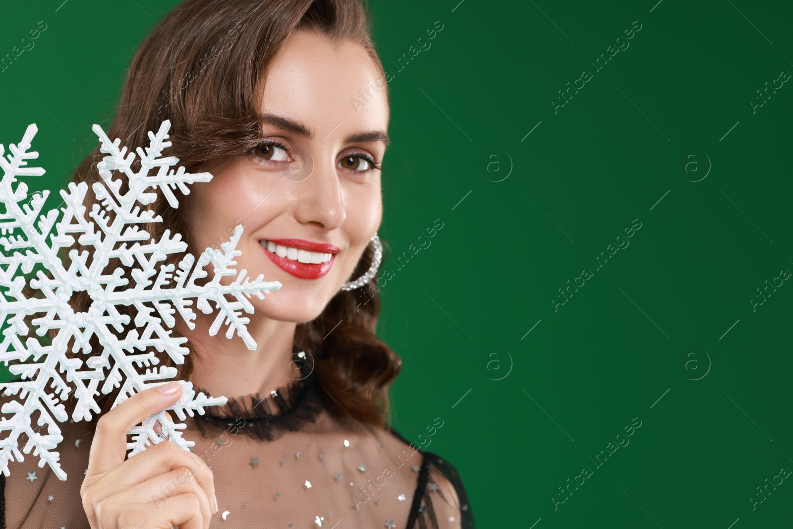 Photo of Smiling woman with perfect makeup holding decorative snowflake on green background, space for text. Christmas celebration